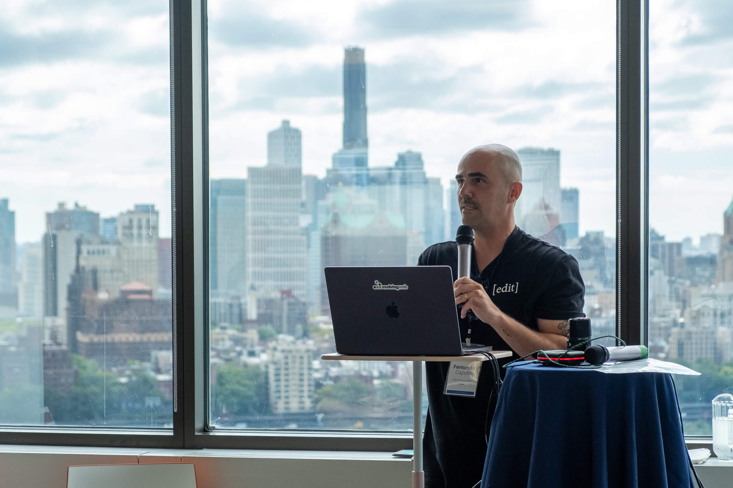 Speaker presenting with a laptop against an NYC skyline backdrop