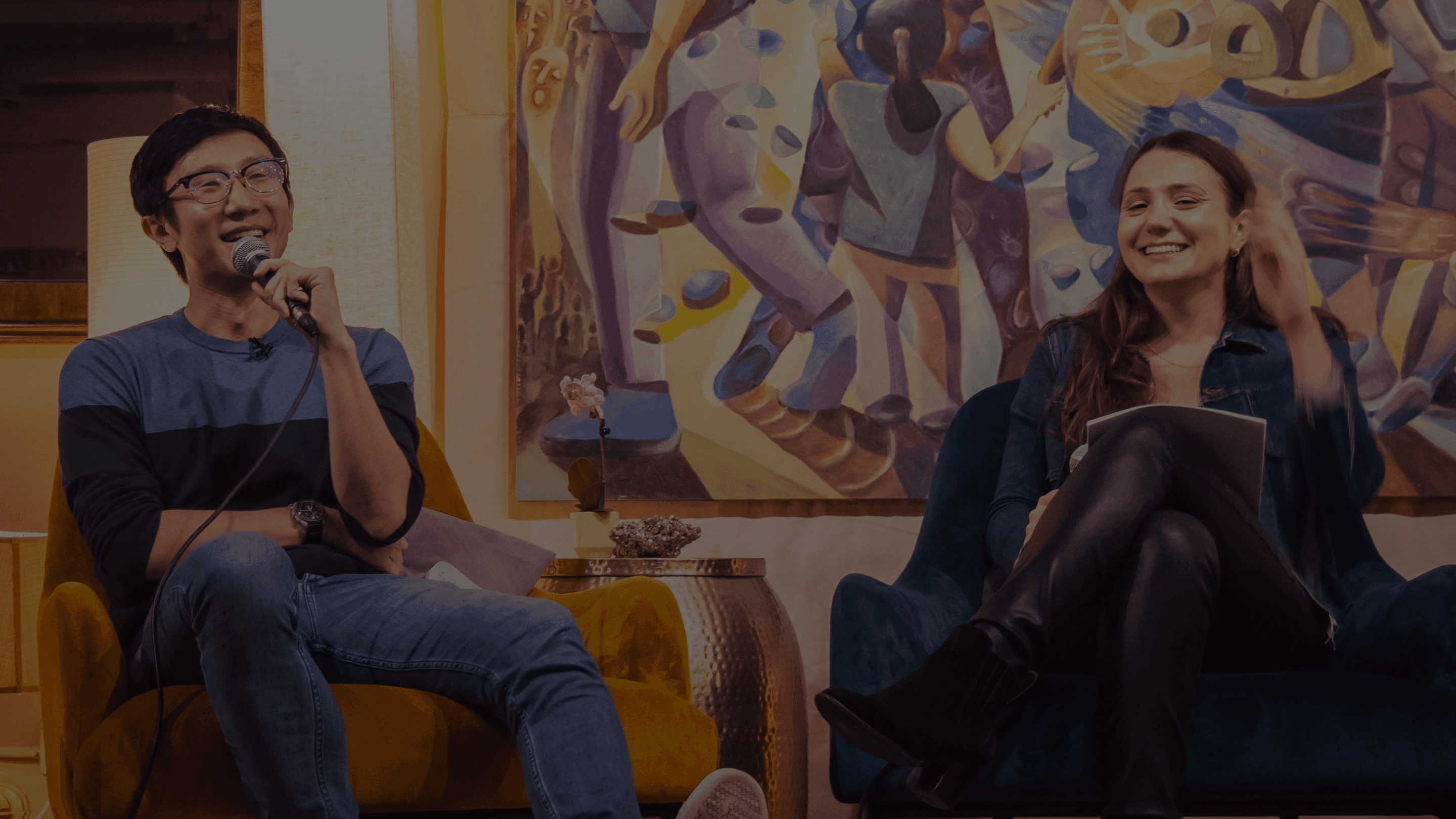 Speaker with a microphone and a host laughing in armchairs at a small San Francisco event.