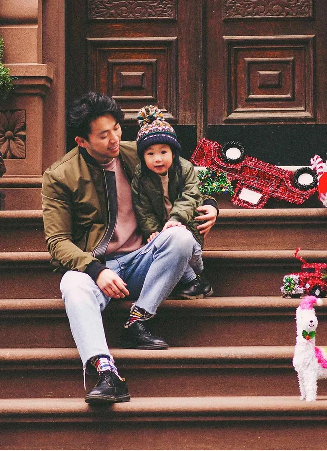 Dr. Tony Lin, board-certified orthodontist, sitting on brownstone steps in Manhattan with a young child