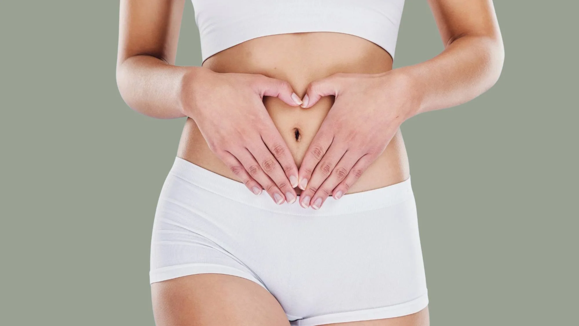 Woman forming a heart shape over her abdomen on a sage green background