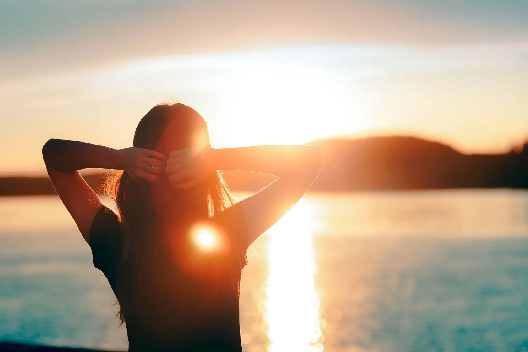 Megan Fernandez in silhouette facing a golden sunset over water