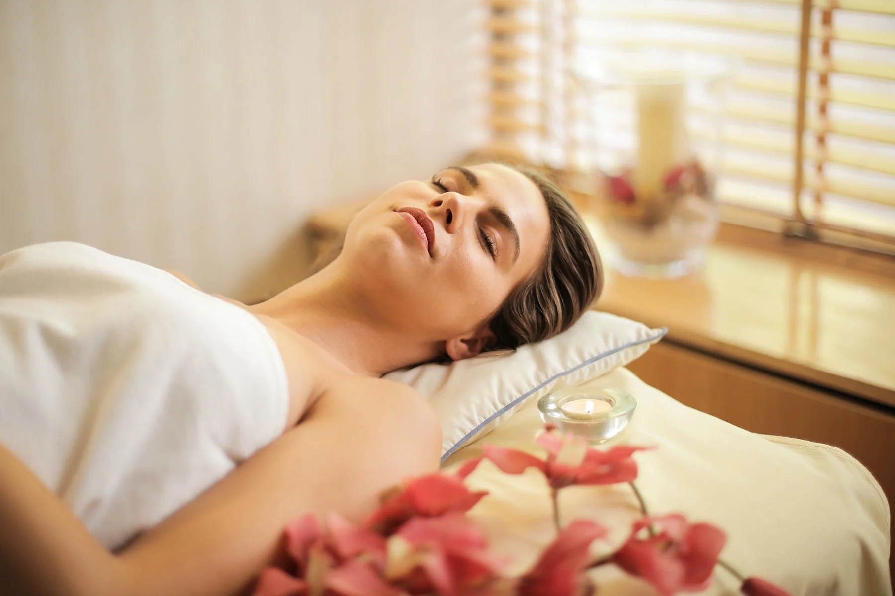Woman relaxing on a spa treatment table with candles and orchids