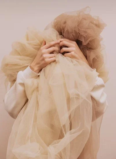 Person holding beige tulle fabric over their head.