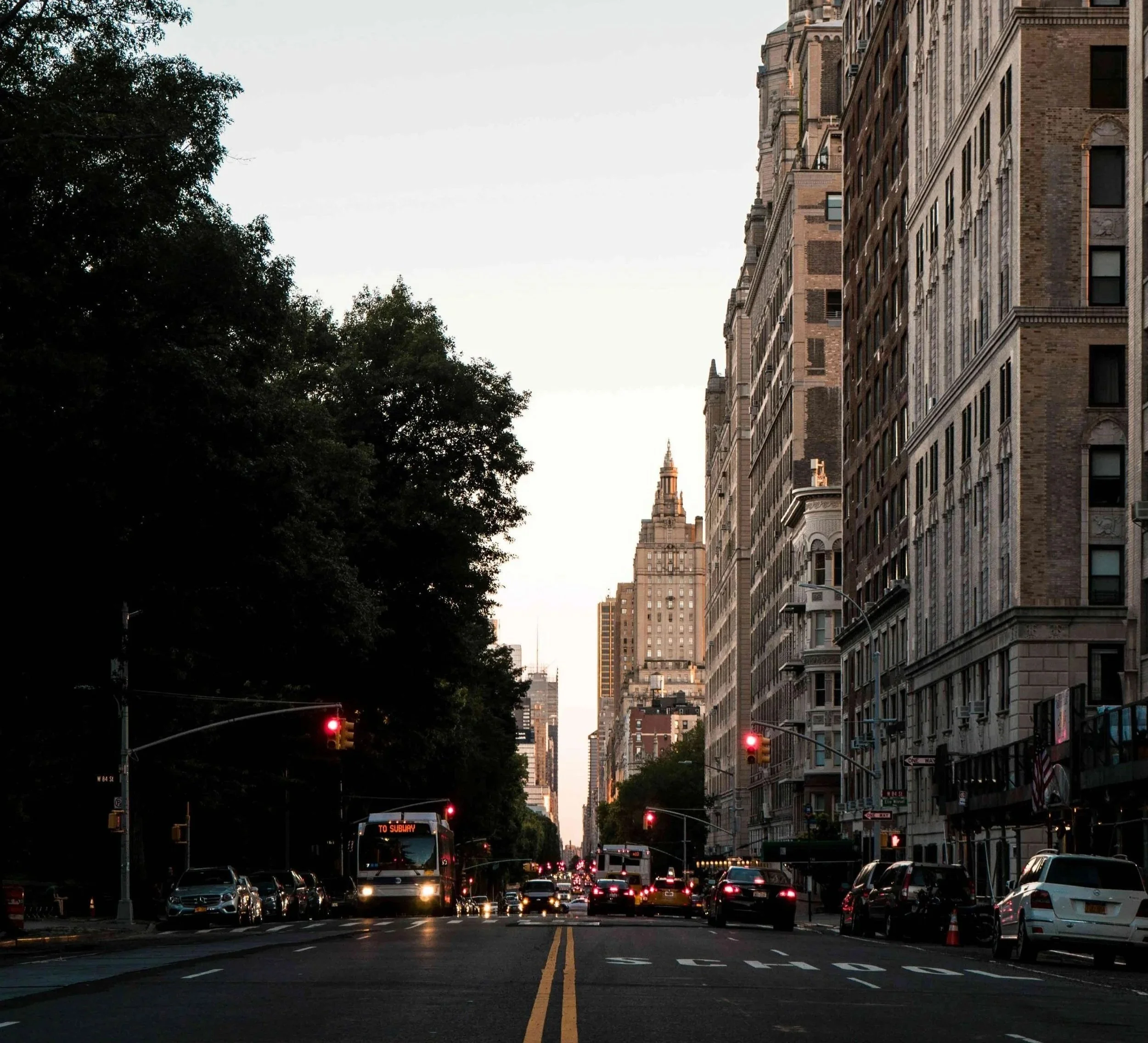 Dusk view of a Manhattan avenue lined with pre-war apartment buildings and trees.