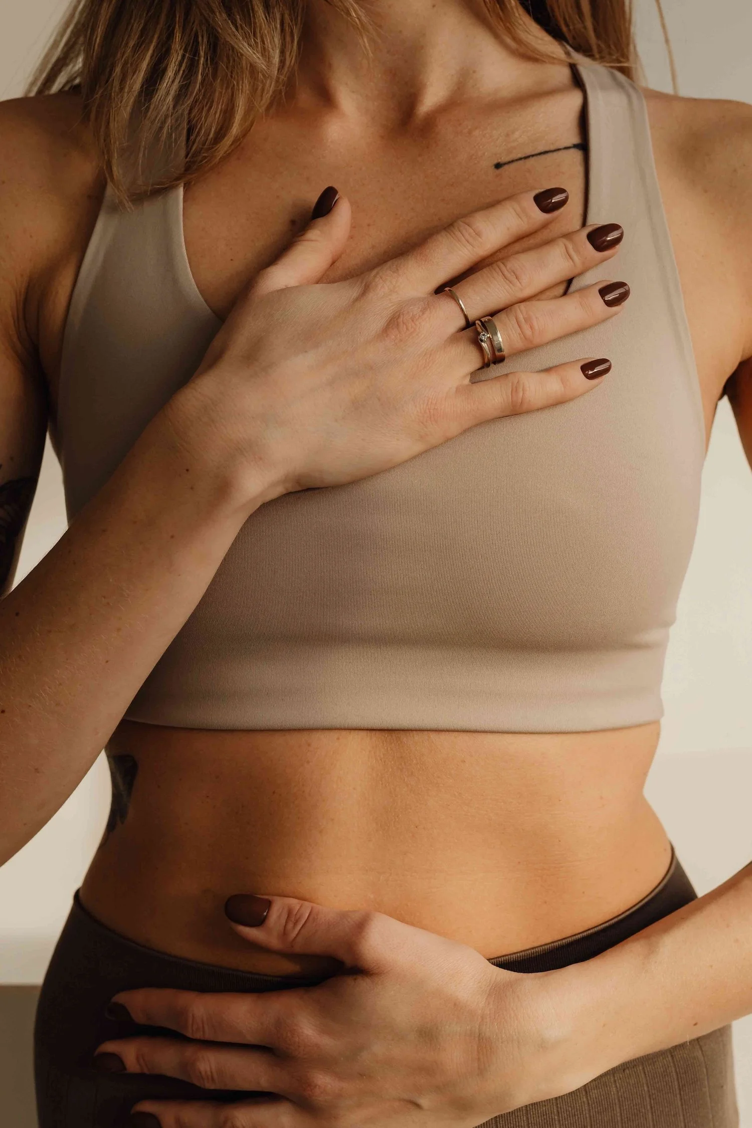 Woman's torso in a beige crop top with her hands resting on her chest and abdomen.