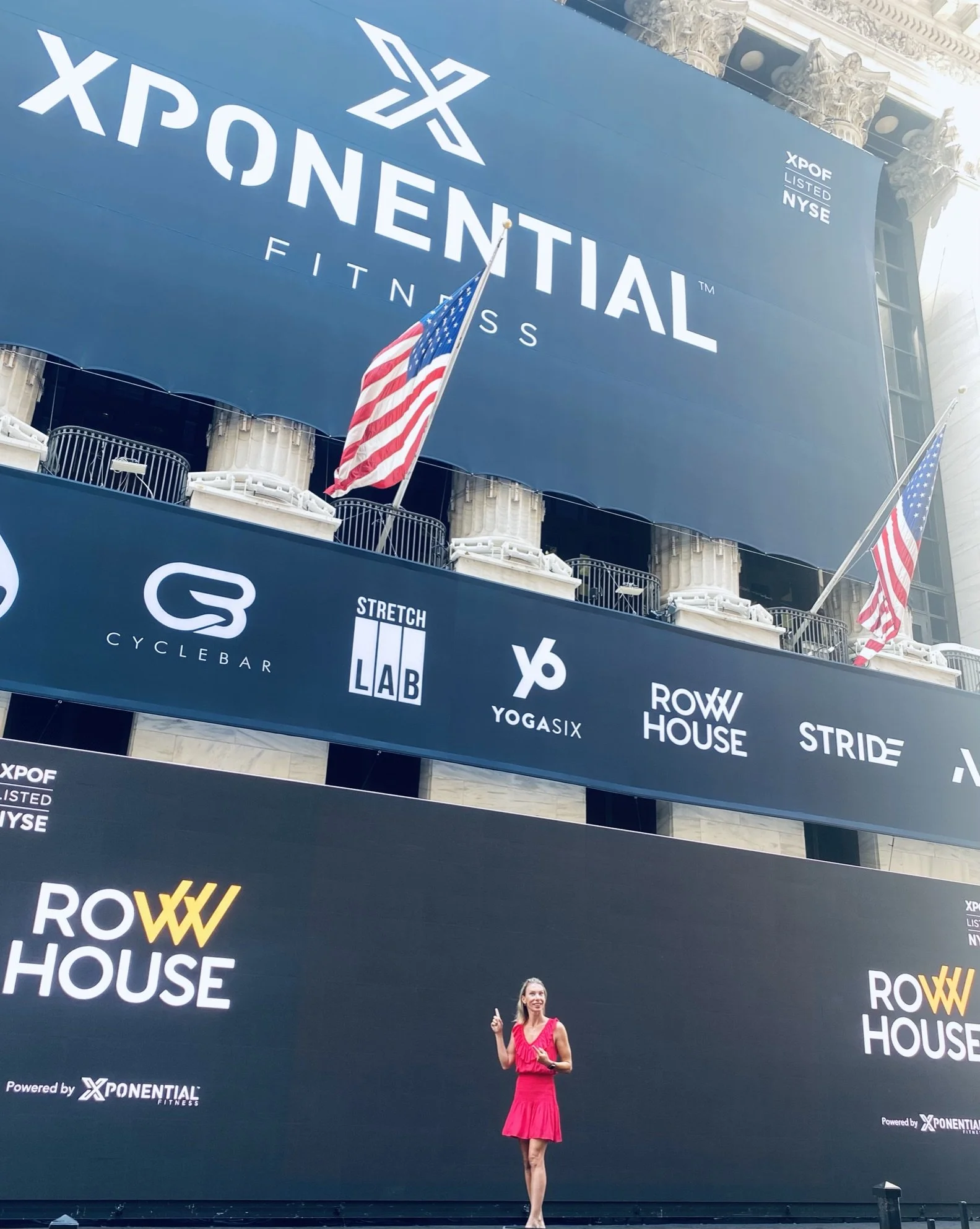 Debra Strougo in a pink dress beneath the Xponential Fitness NYSE IPO banner outside the New York Stock Exchange
