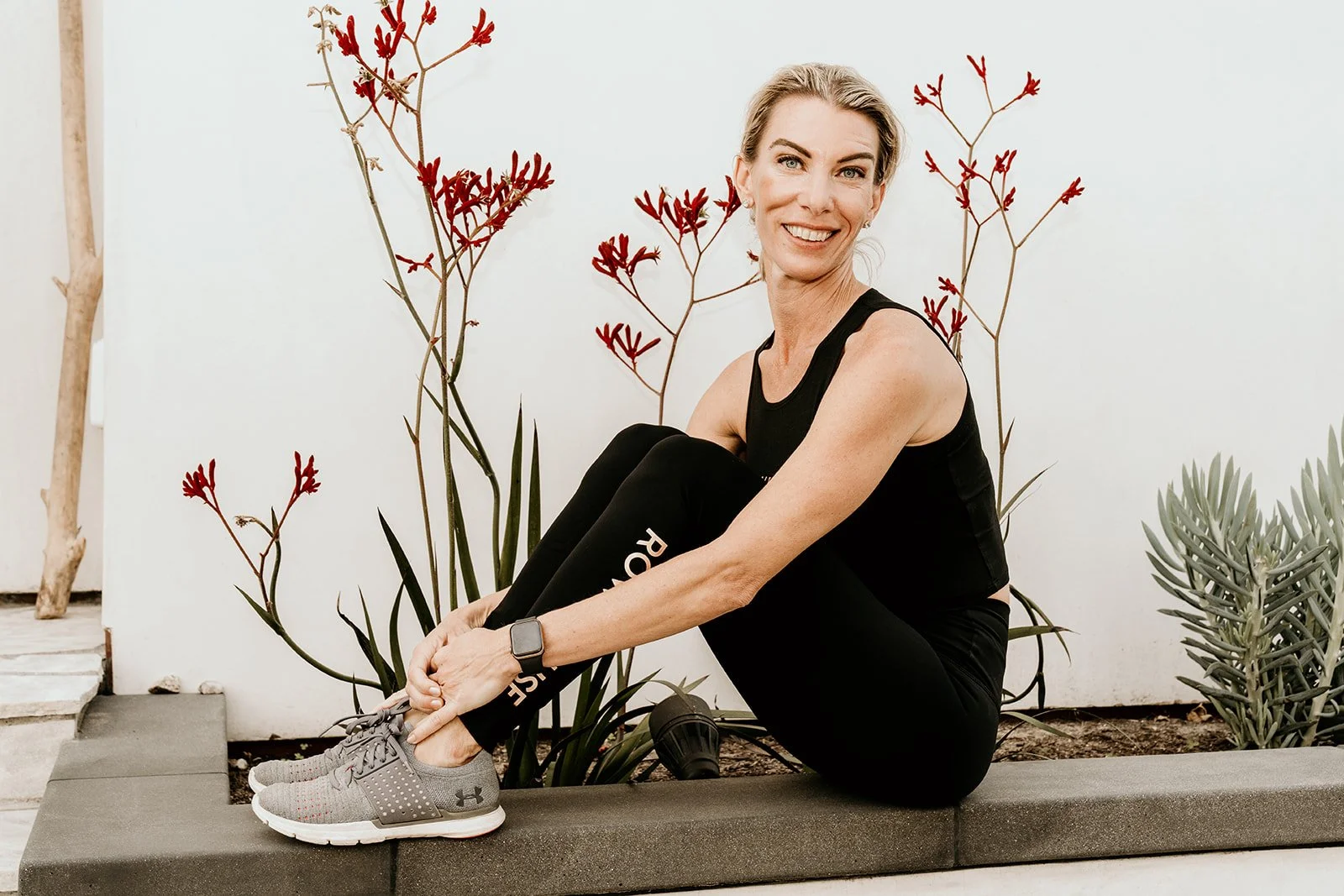 Debra Strougo seated on a ledge outdoors smiling at the camera in Row House athletic wear
