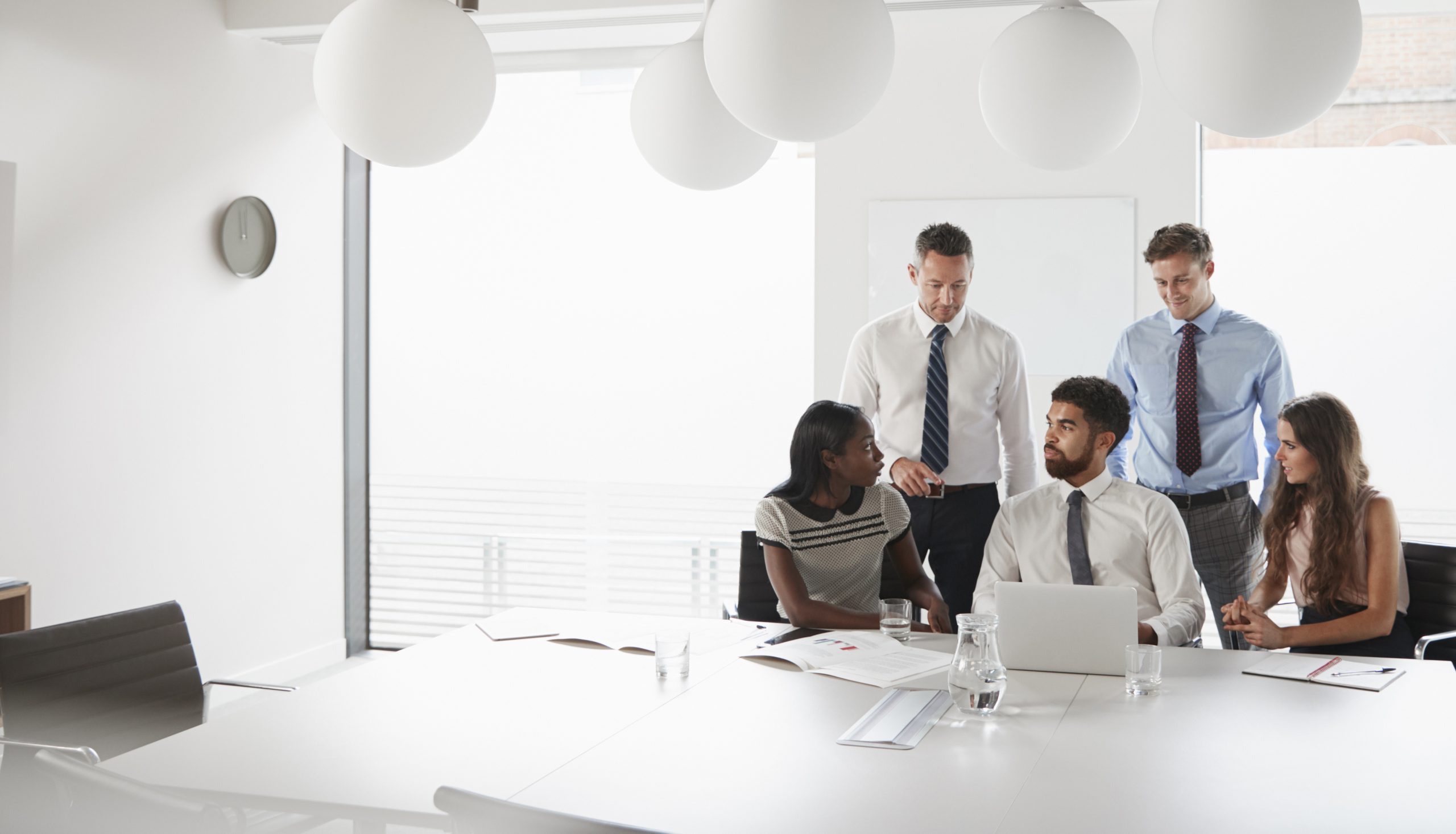 Five business professionals collaborating around a conference table in a bright modern boardroom.