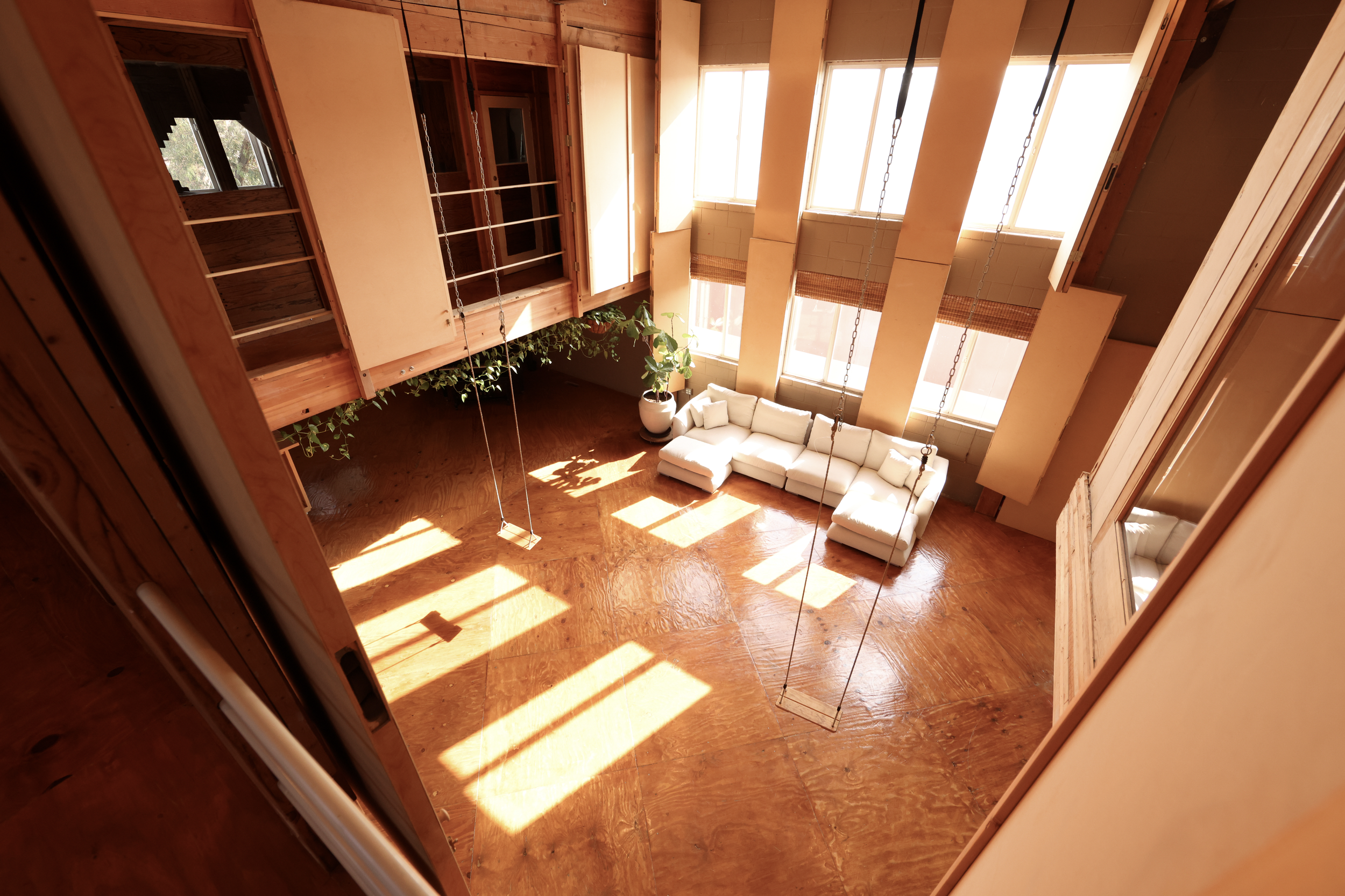 Loft East — sun-filled high-ceiling loft with herringbone floors, hanging chain swings, and tall bamboo-shaded windows