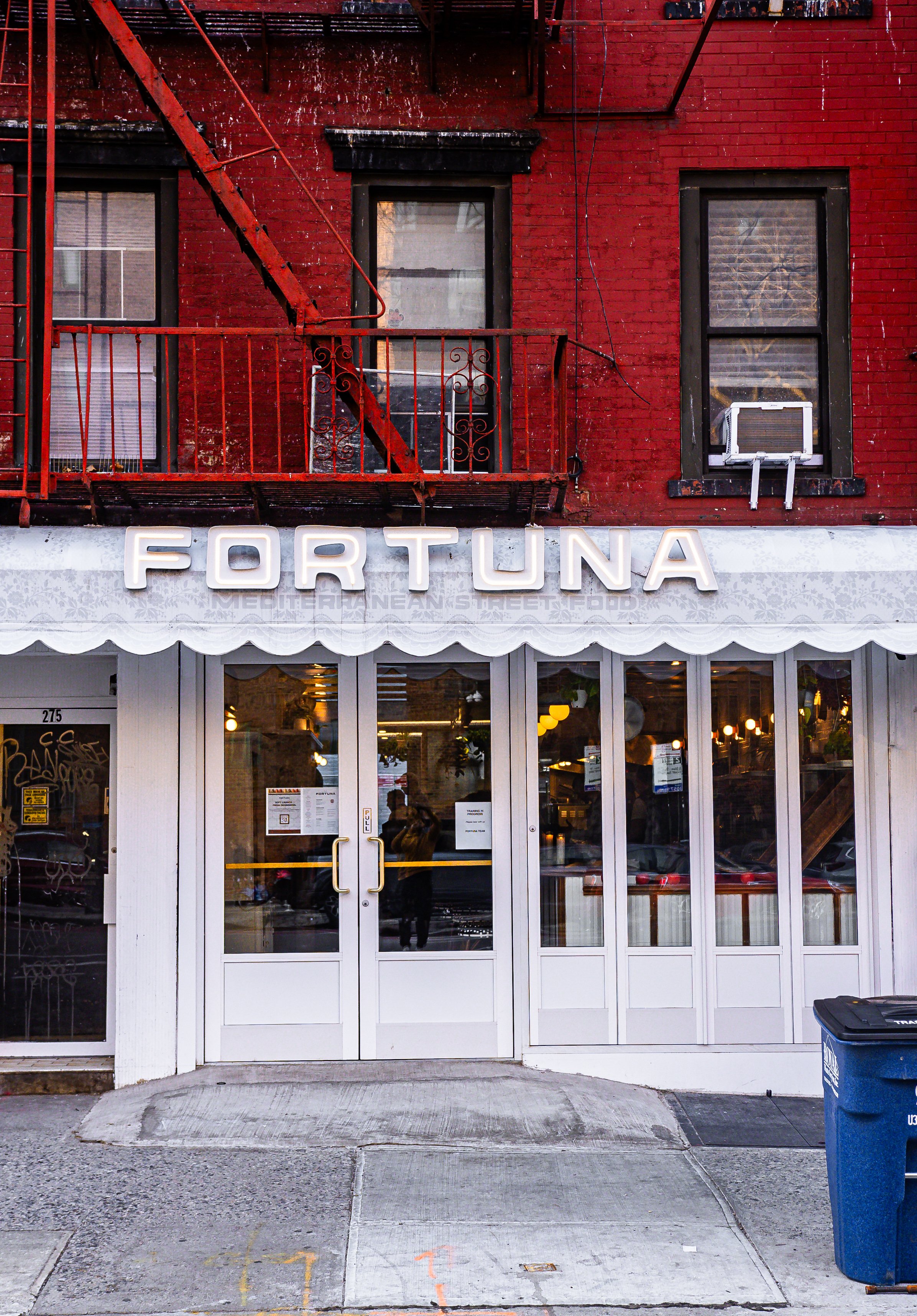 Storefront with white entrance doors and large glass windows, sign reading 'Fortuna', street sidewalk with marked parking spots.