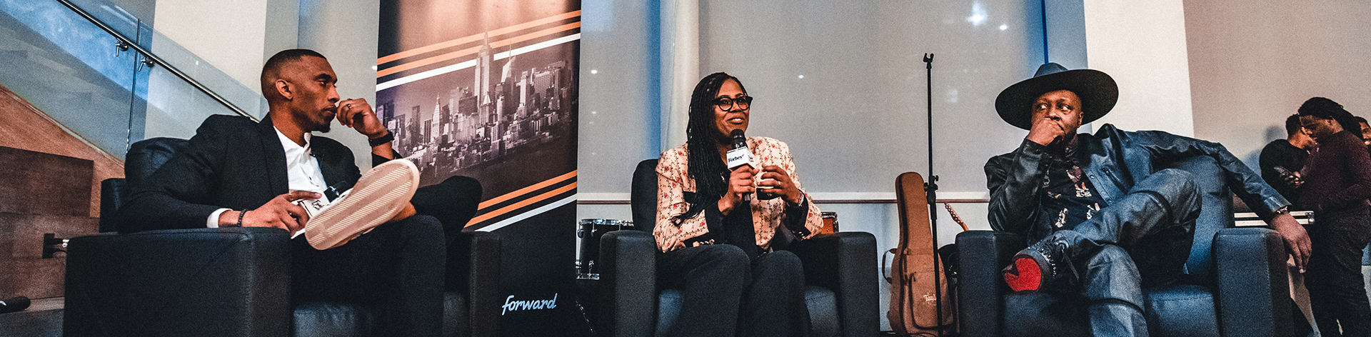 Three people on stage at a panel event with a Fueled by Culture backdrop