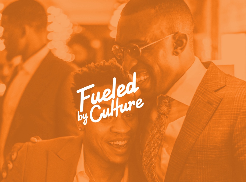 Orange-tinted still of two people at an event with the Fueled by Culture wordmark overlaid
