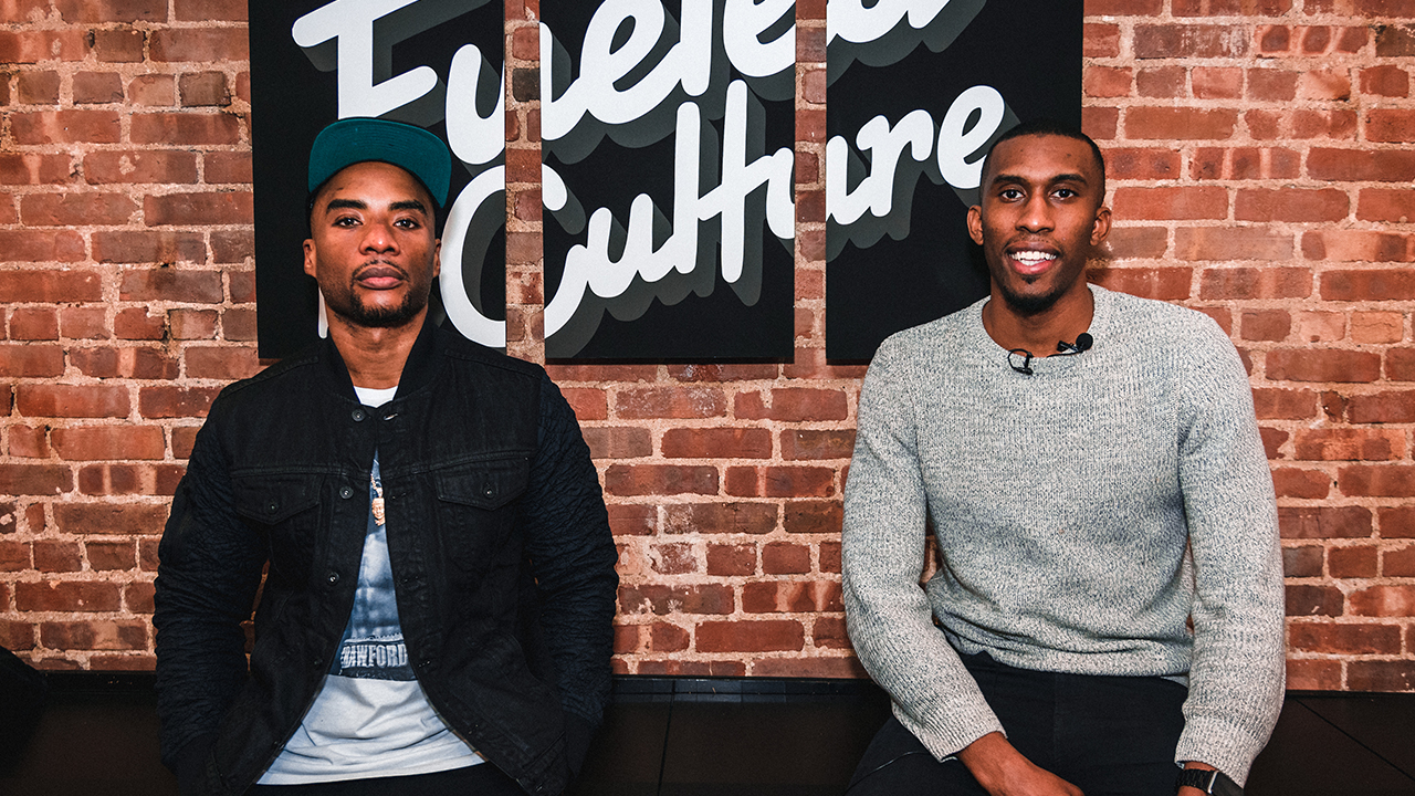 Two men seated side by side in front of a brick wall with Fueled by Culture signage