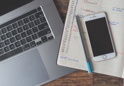 Laptop, smartphone and an open planner with a pen on a wooden desk