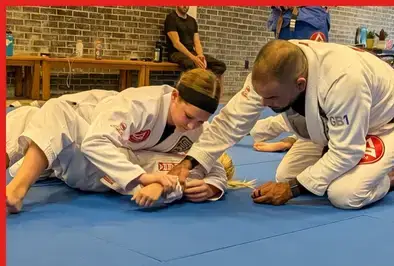 Female student in a white gi drilling a ground technique with an instructor
