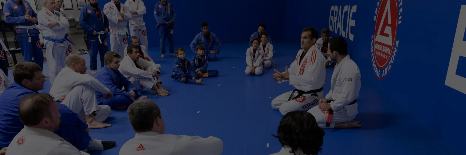 Teens and adults seated in a class circle on the blue mats while the instructor teaches
