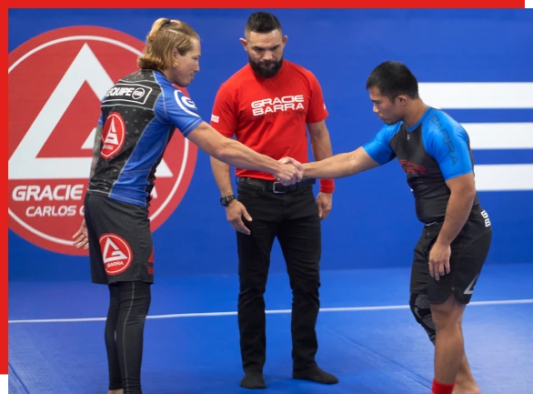 Two competitors shaking hands with a Gracie Barra referee on a competition mat