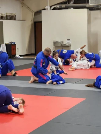 Instructor and children grappling on red and grey mats