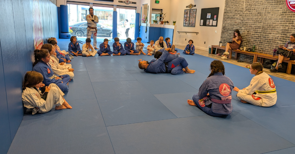 Kids' class watching two students spar while the instructor supervises