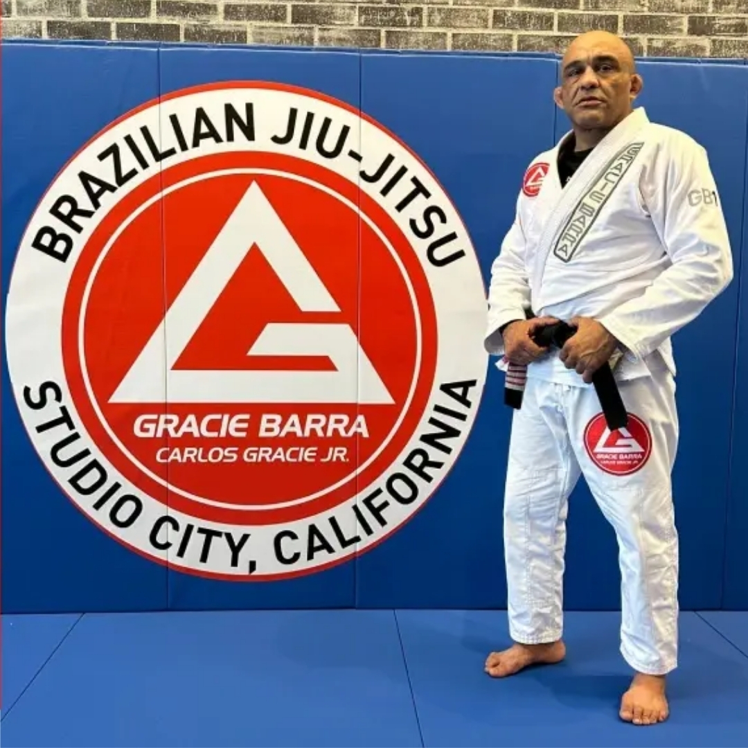 Rodrigo Costa, black belt in a white gi, in front of the Gracie Barra Studio City California wall logo