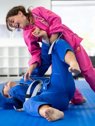 Girl in a pink gi working a ground technique on another child in a blue gi