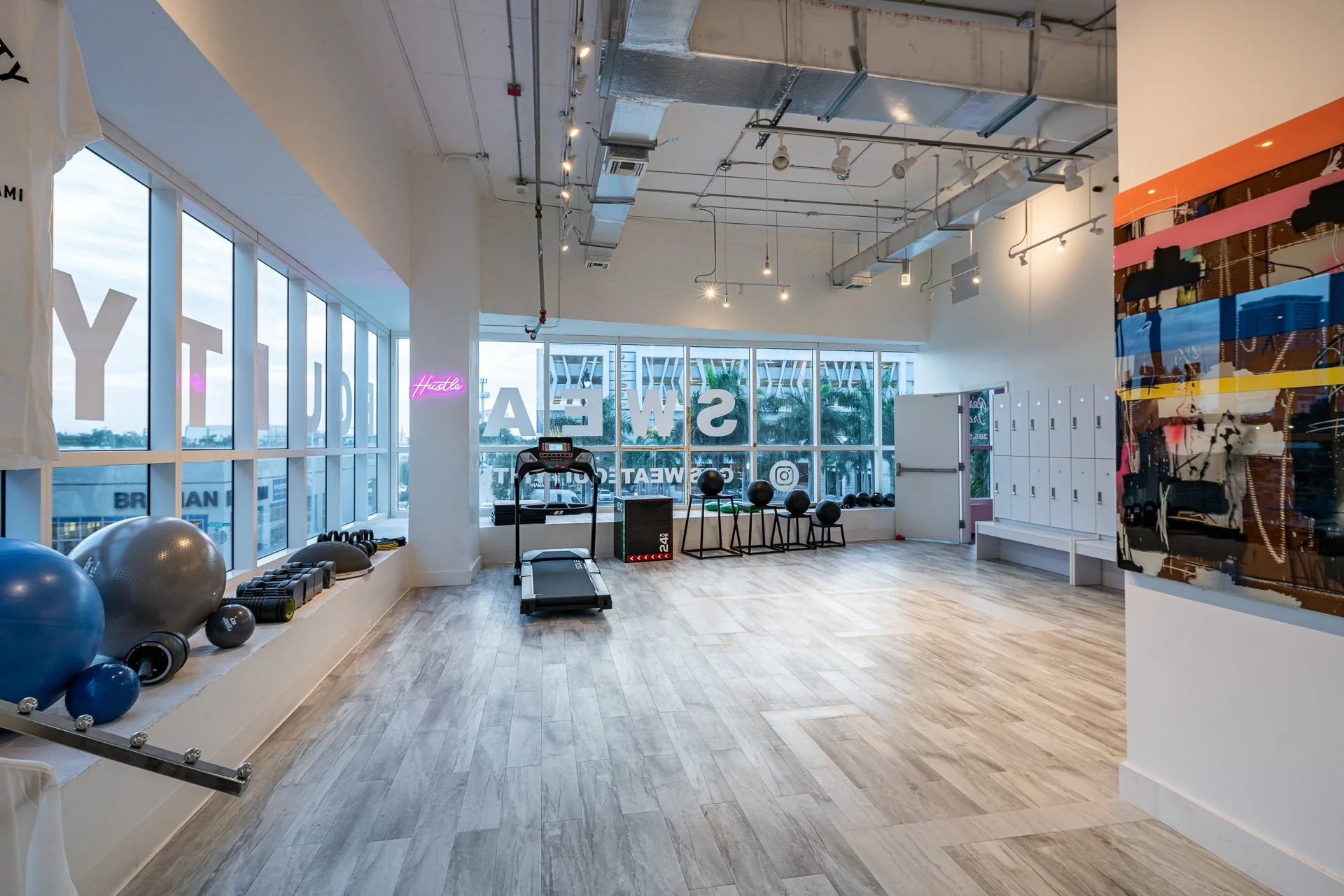 Sweat Equity Fitness gym interior with window lettering and neon Hustle sign