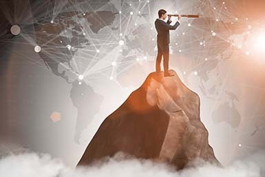 A businessman with a telescope on a rocky peak overlaid with a global network graphic