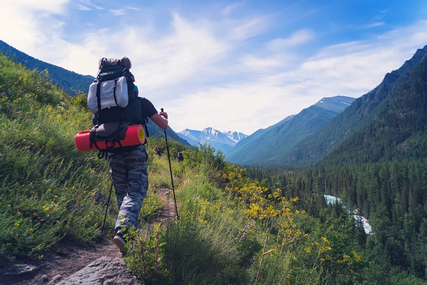 Lone backpacker hiking down a lush mountain valley trail with a river below