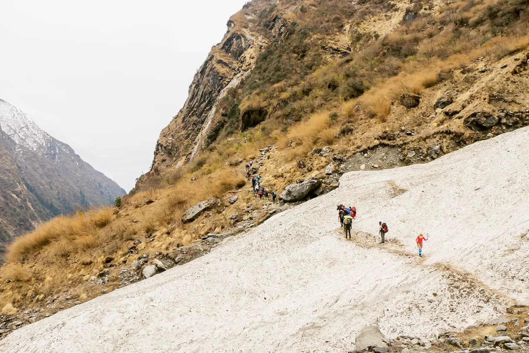 Group of trekkers ascending a snowy mountain trail in a rocky valley