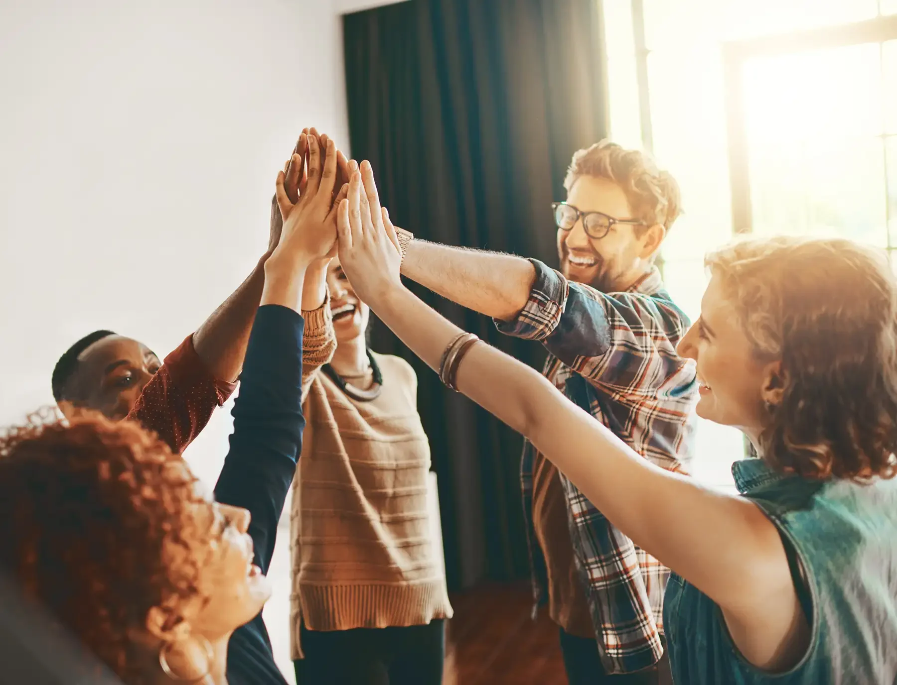 Diverse group of people high-fiving in a circle indoors