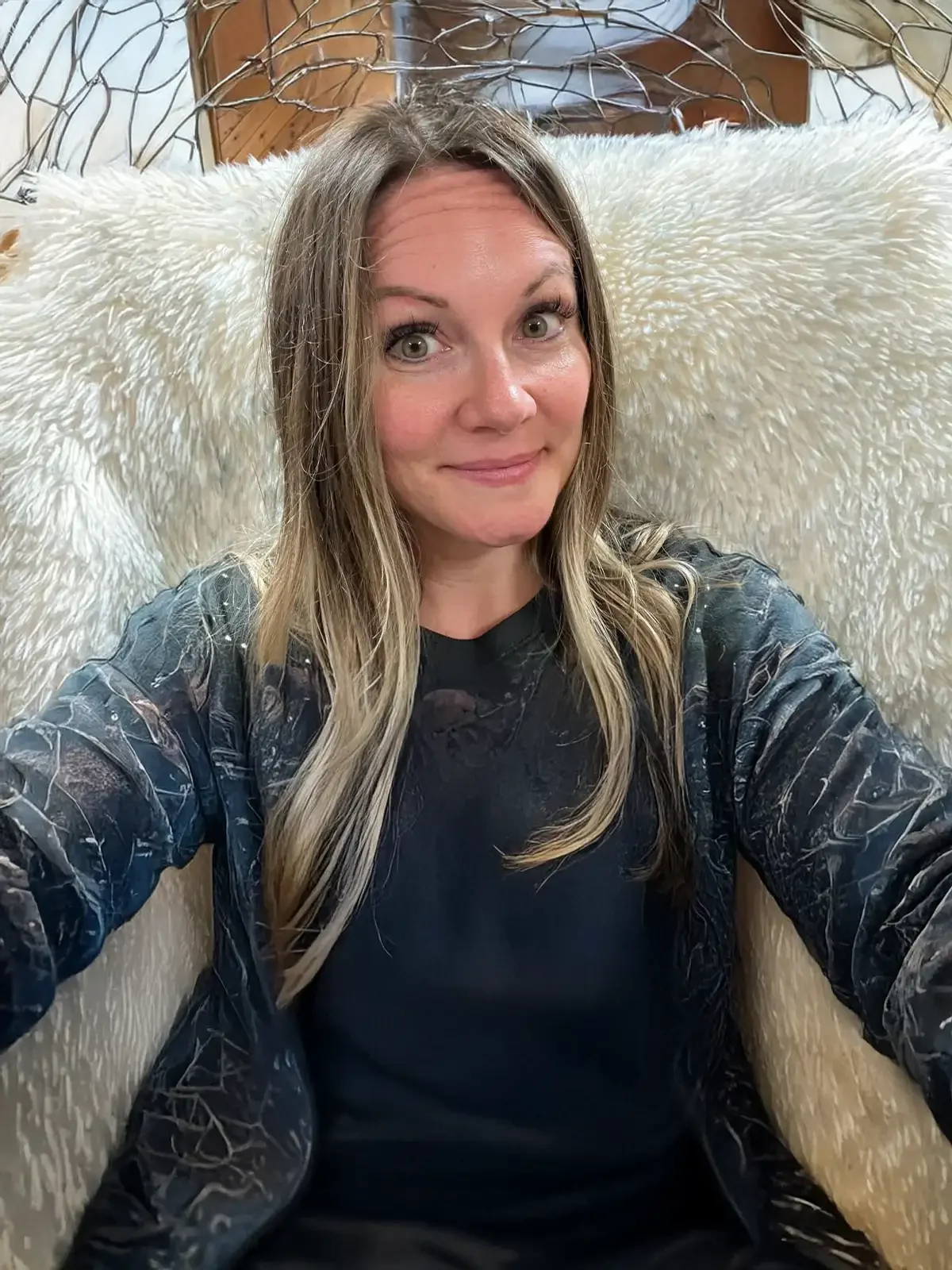 Jenni Lee, smiling with blonde highlights, seated in a fluffy white chair