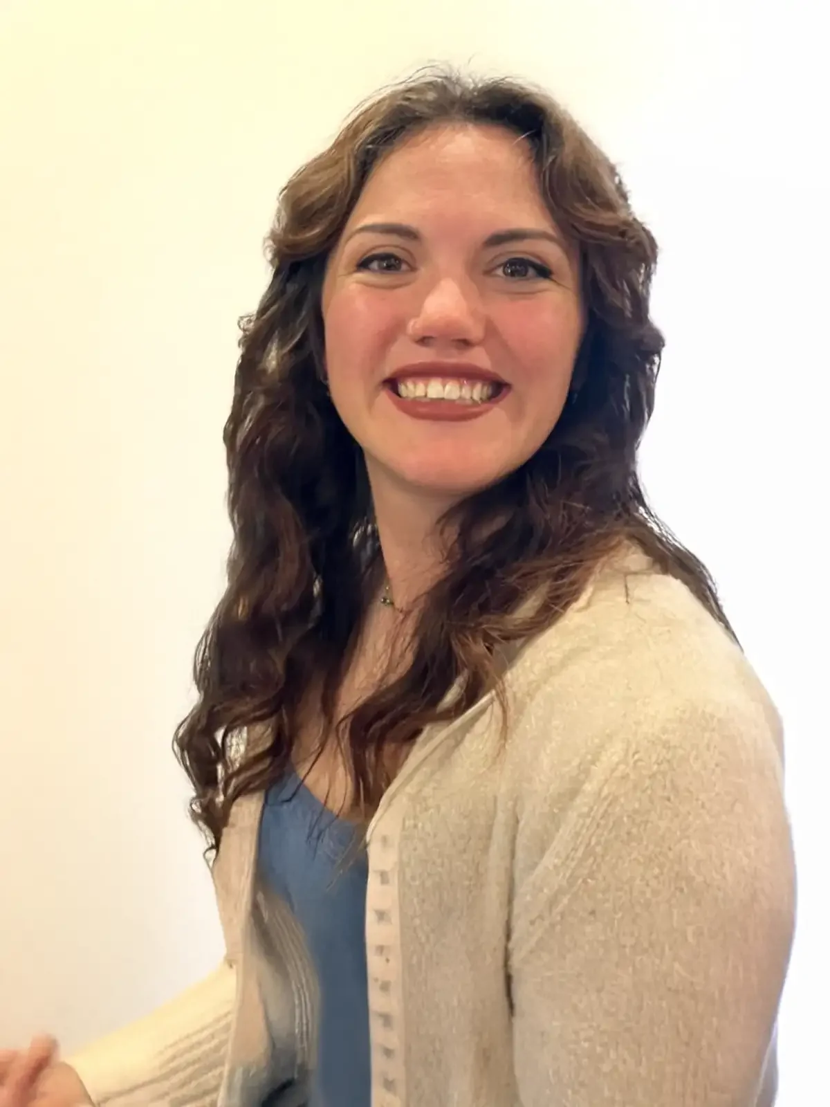 Casey Brandts, smiling with curly brown hair in a beige cardigan
