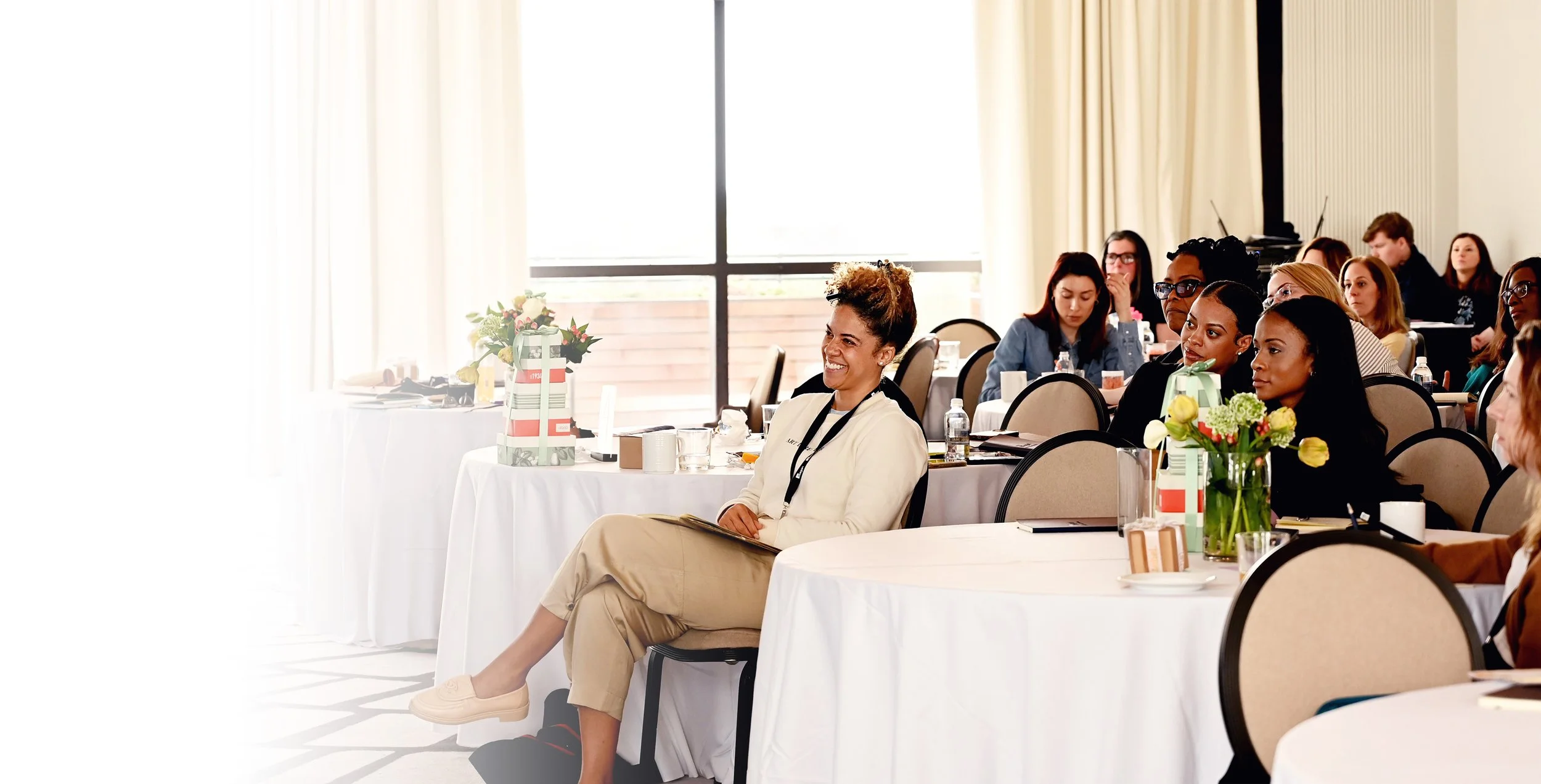Women at a Lofti corporate retreat in a bright ballroom with round tables and floral centerpieces
