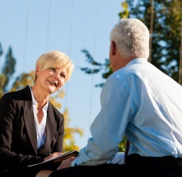 An executive coach with a notepad in conversation with a senior leader outdoors