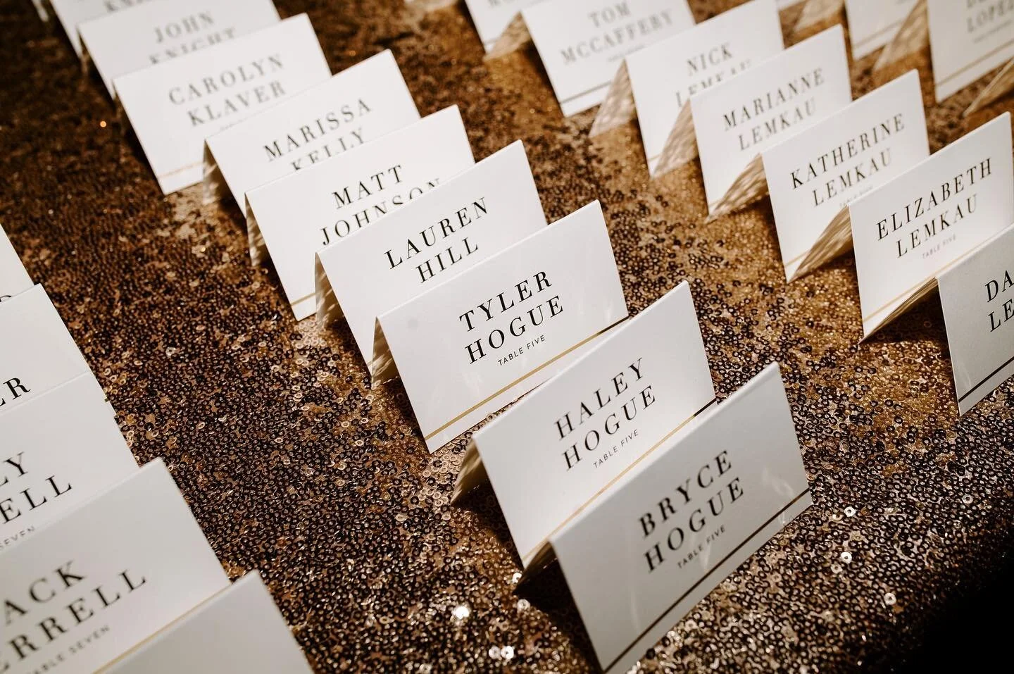 Wedding escort cards displayed on a gold sequin tablecloth