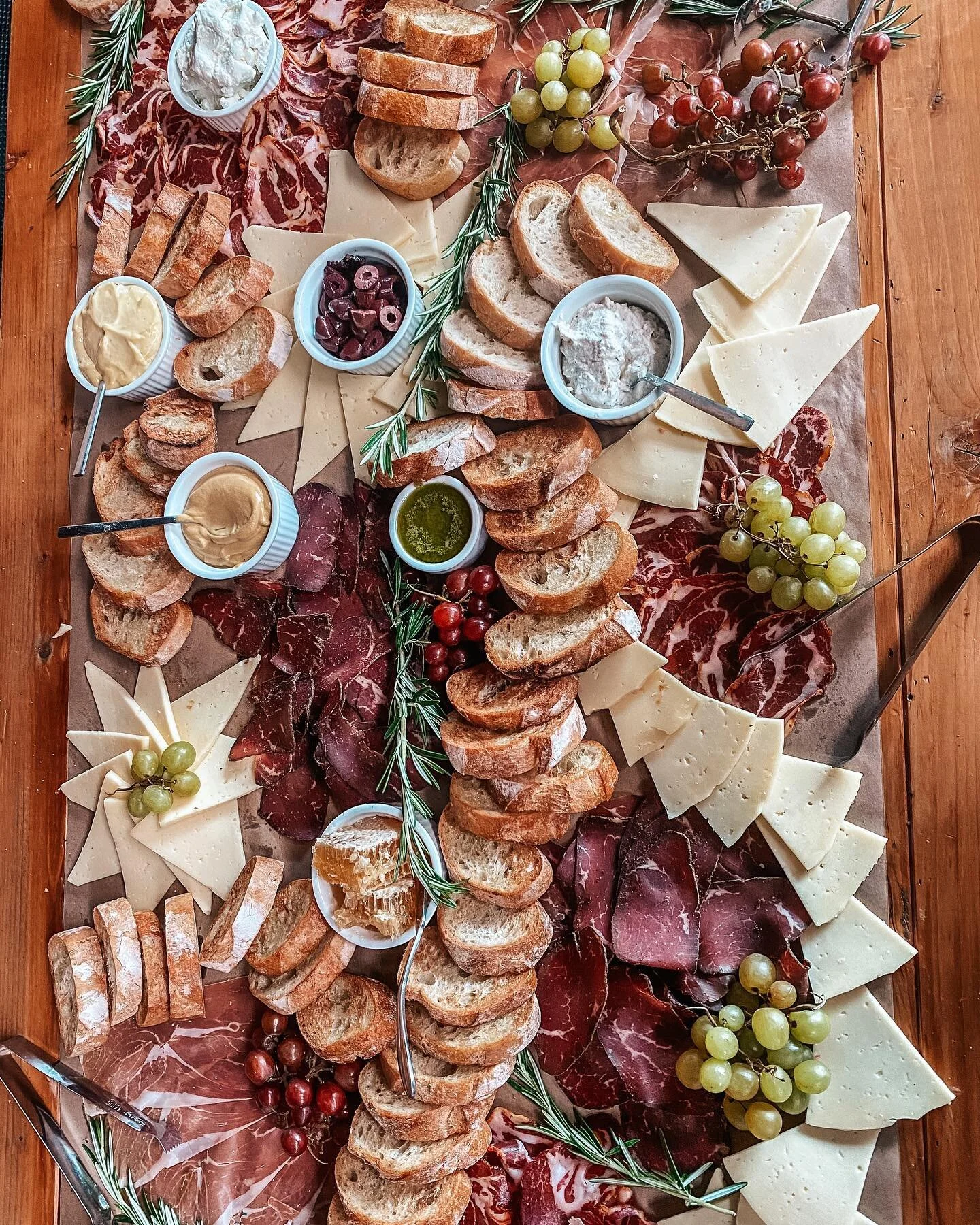 Large charcuterie and grazing board with meats, cheeses, bread, grapes, and dips viewed from above