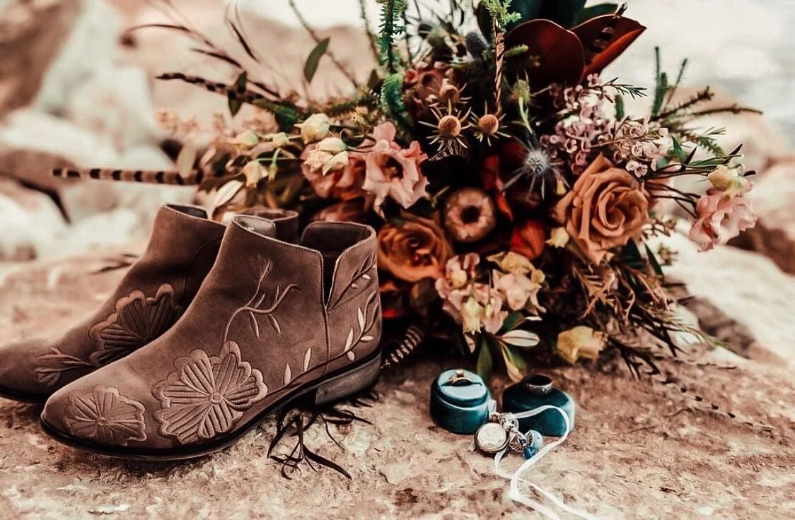 Boho wedding flat-lay with ankle boots, a bouquet, ring boxes, and a pocket watch