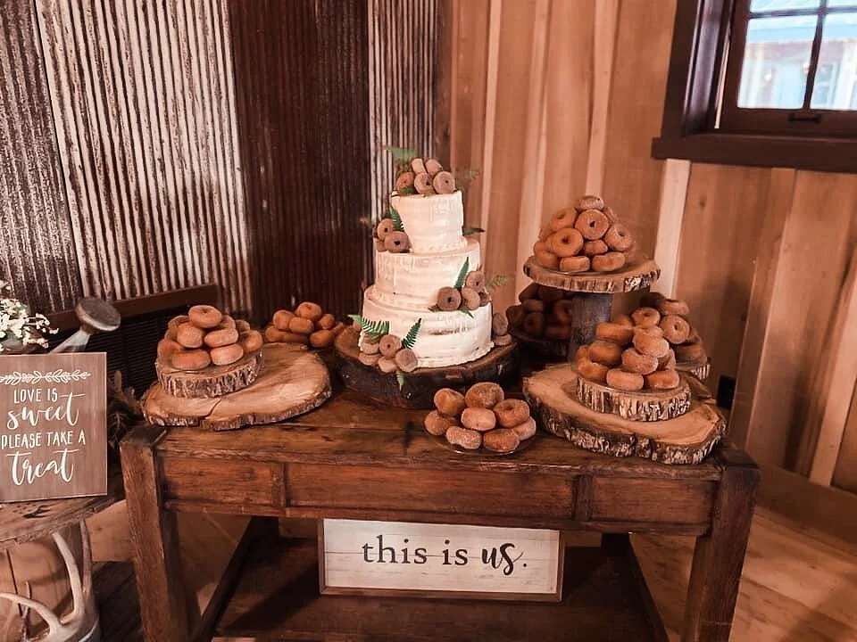 Wider view of a rustic barn dessert table with a naked cake and donuts on wood slices