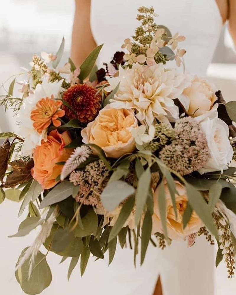 Bride holding a lush peach, orange, and white garden bridal bouquet with dahlias, zinnias, and eucalyptus