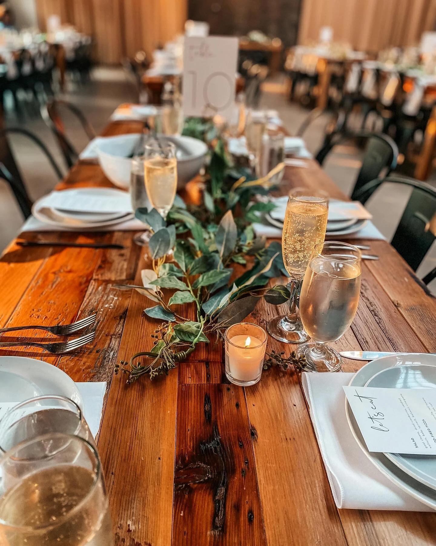 Rustic farm table with eucalyptus garland, champagne flutes, candles, and place settings