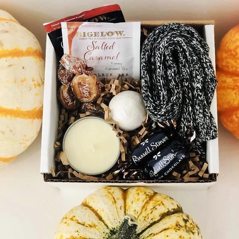 Fall-themed gift box with tea, a candle, and chocolates surrounded by gourds