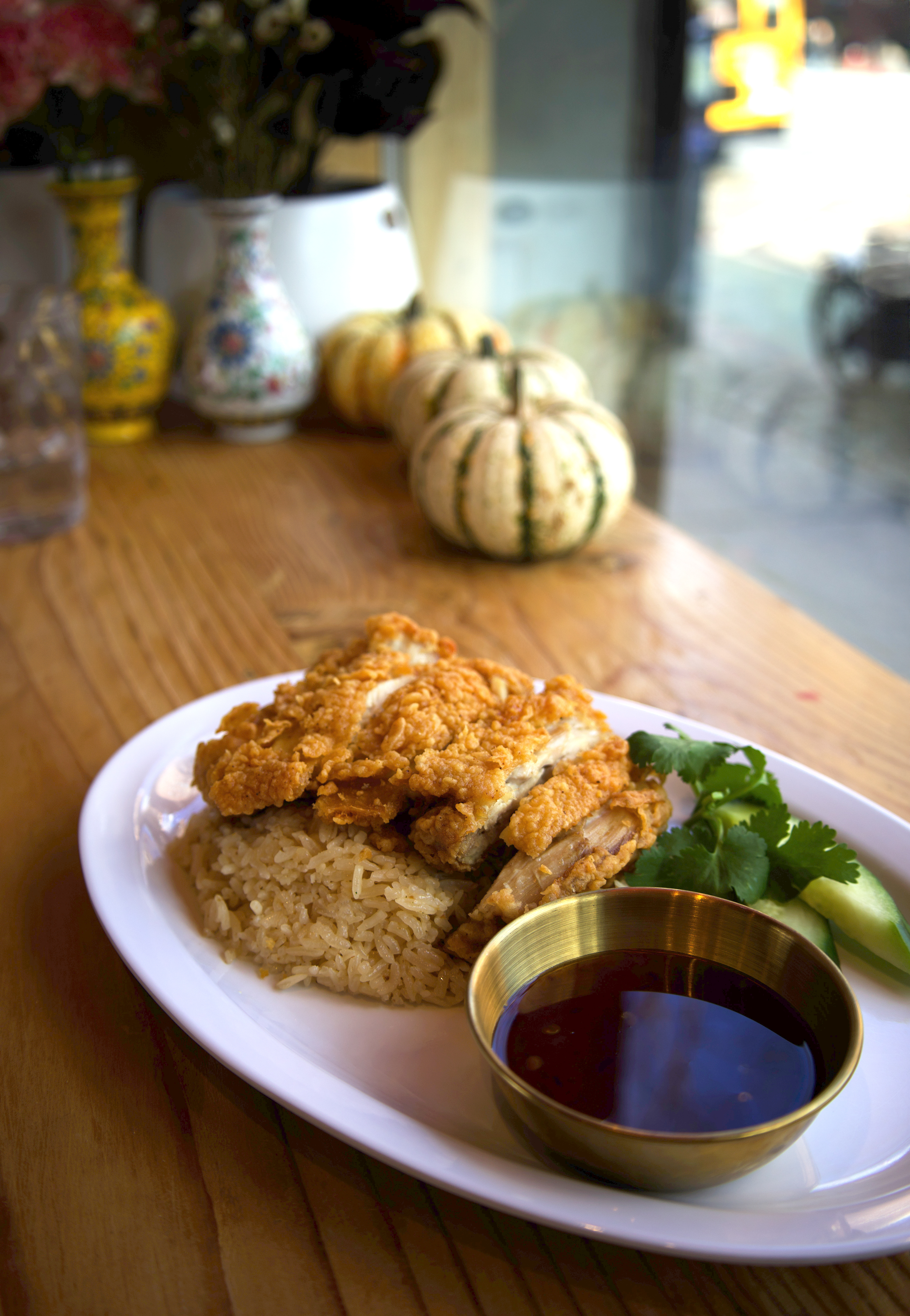 Fried chicken rice plate on a wooden table with pumpkins and a floral vase behind