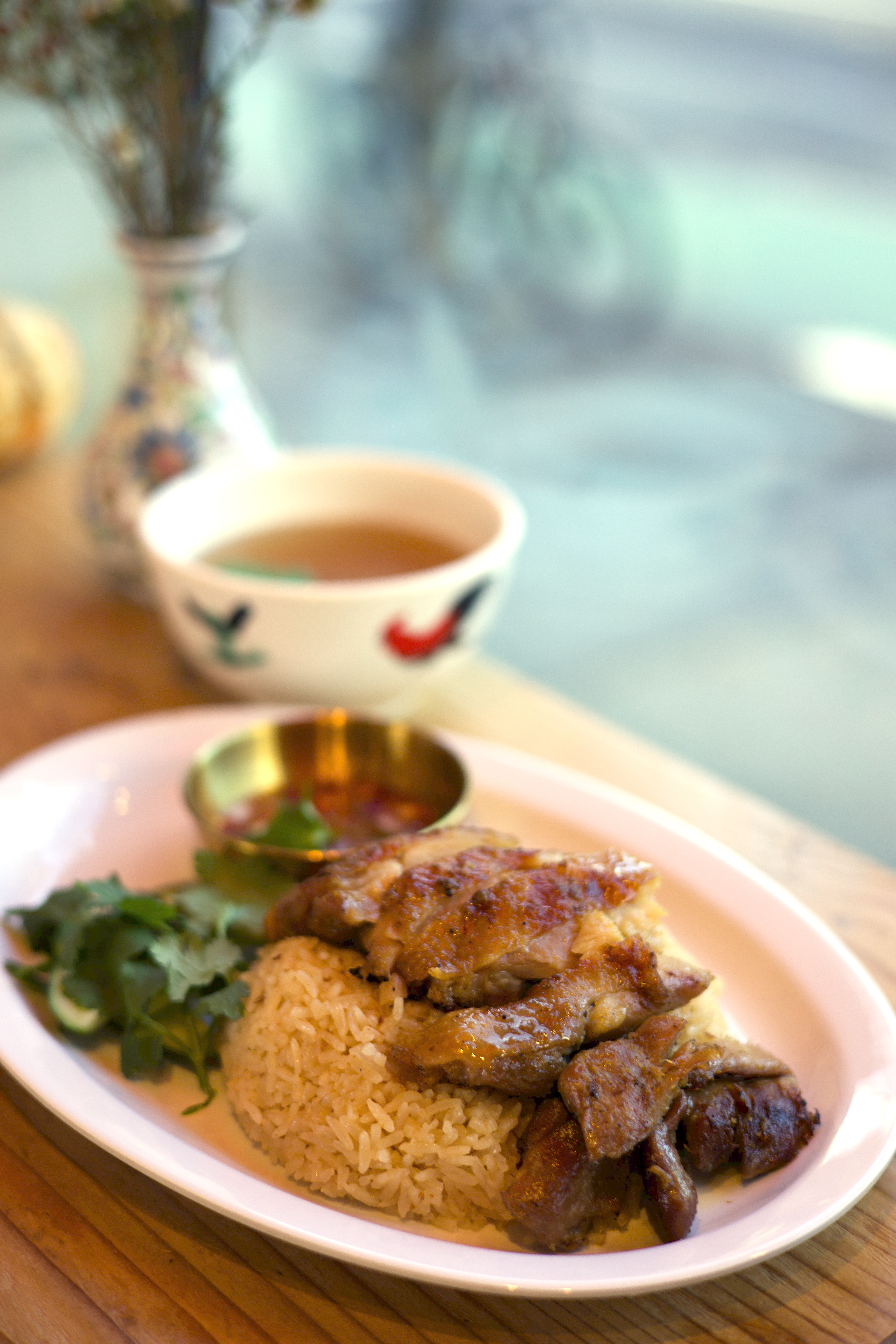 Roasted chicken rice plate with dipping sauce and broth on a wooden table