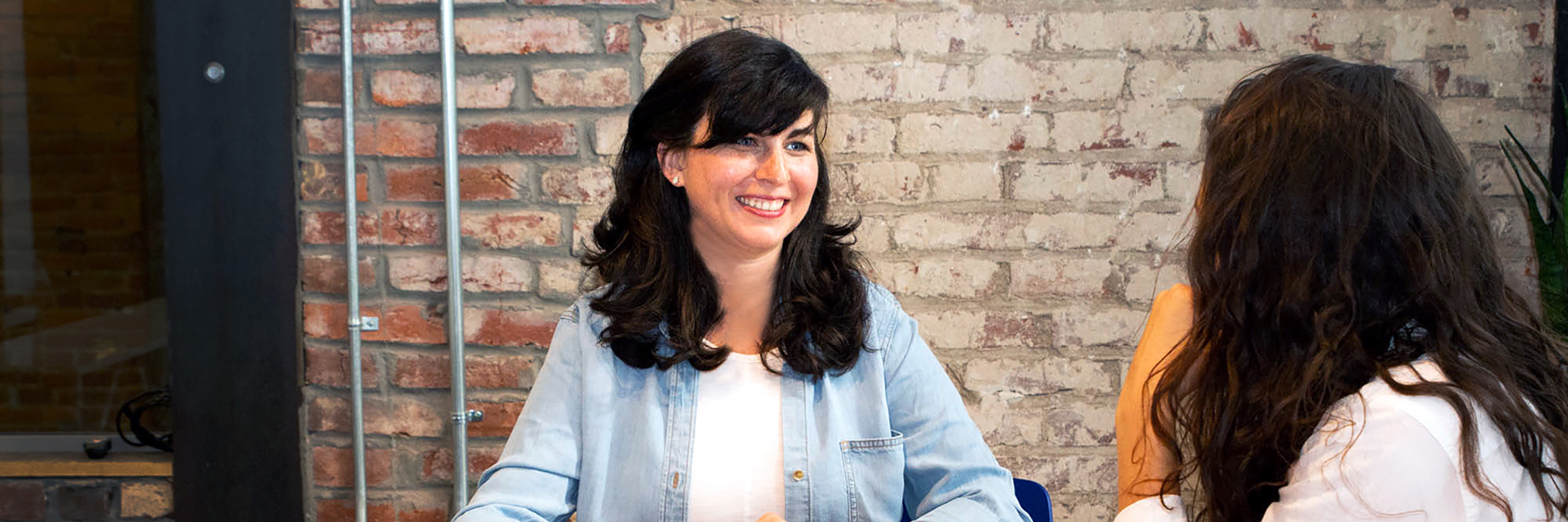 A woman smiling in conversation against an exposed brick wall