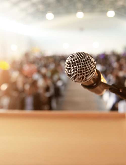 Microphone in front of a blurred audience representing speaking engagements