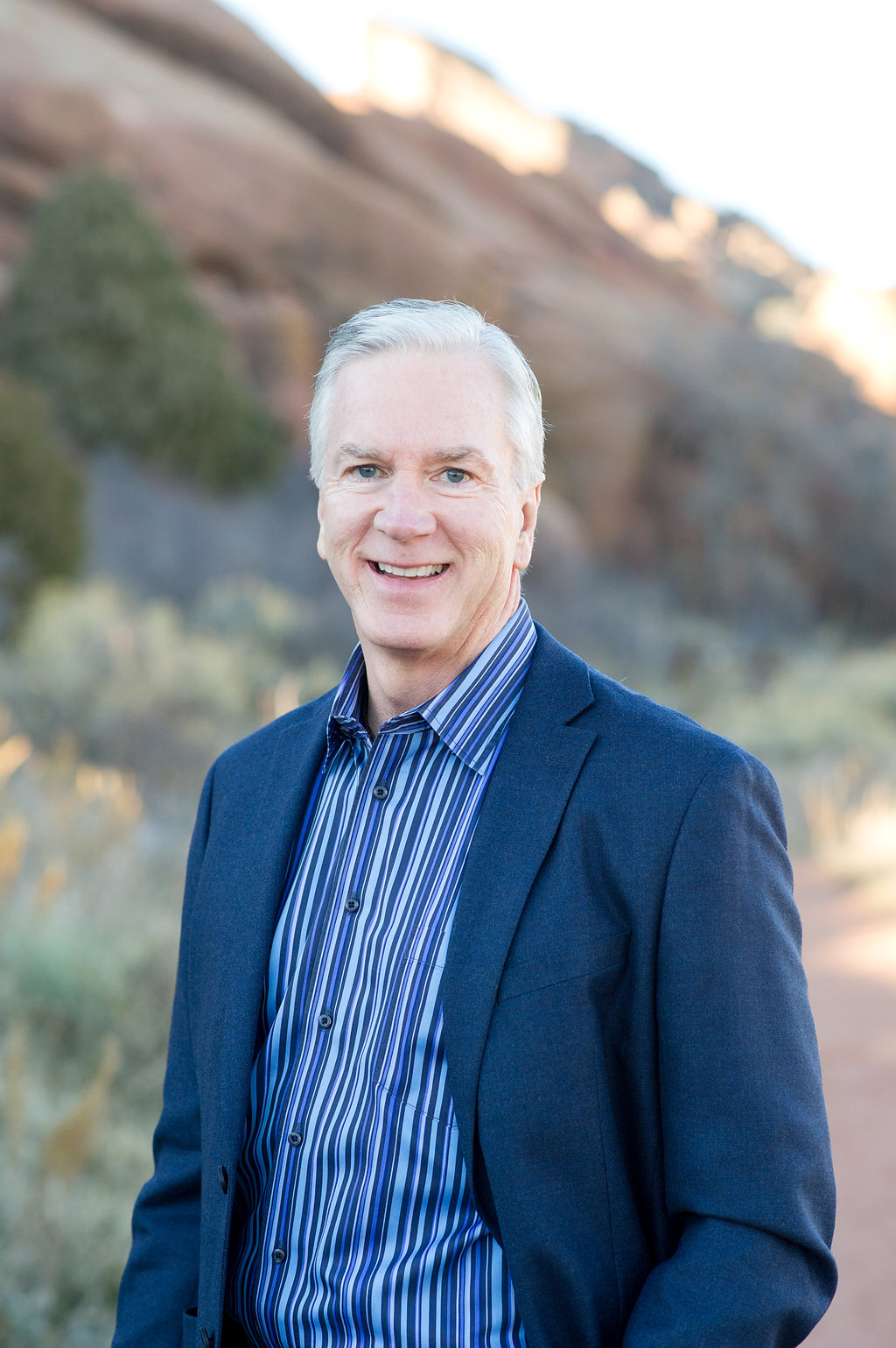 Silver-haired advisor in a blue blazer smiling outdoors against red-rock scenery