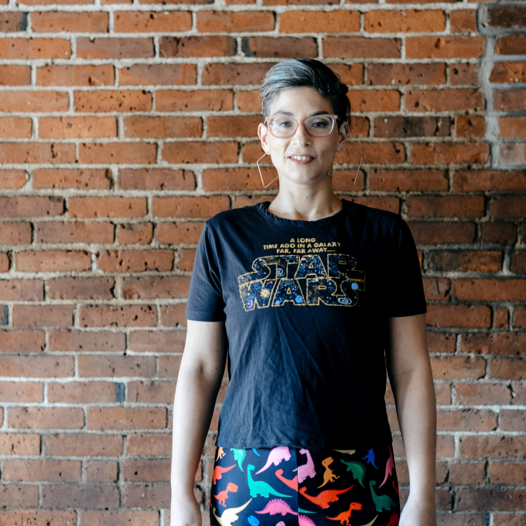 Rachel Dash-Dougherty in a Star Wars t-shirt and printed leggings in front of a brick wall.
