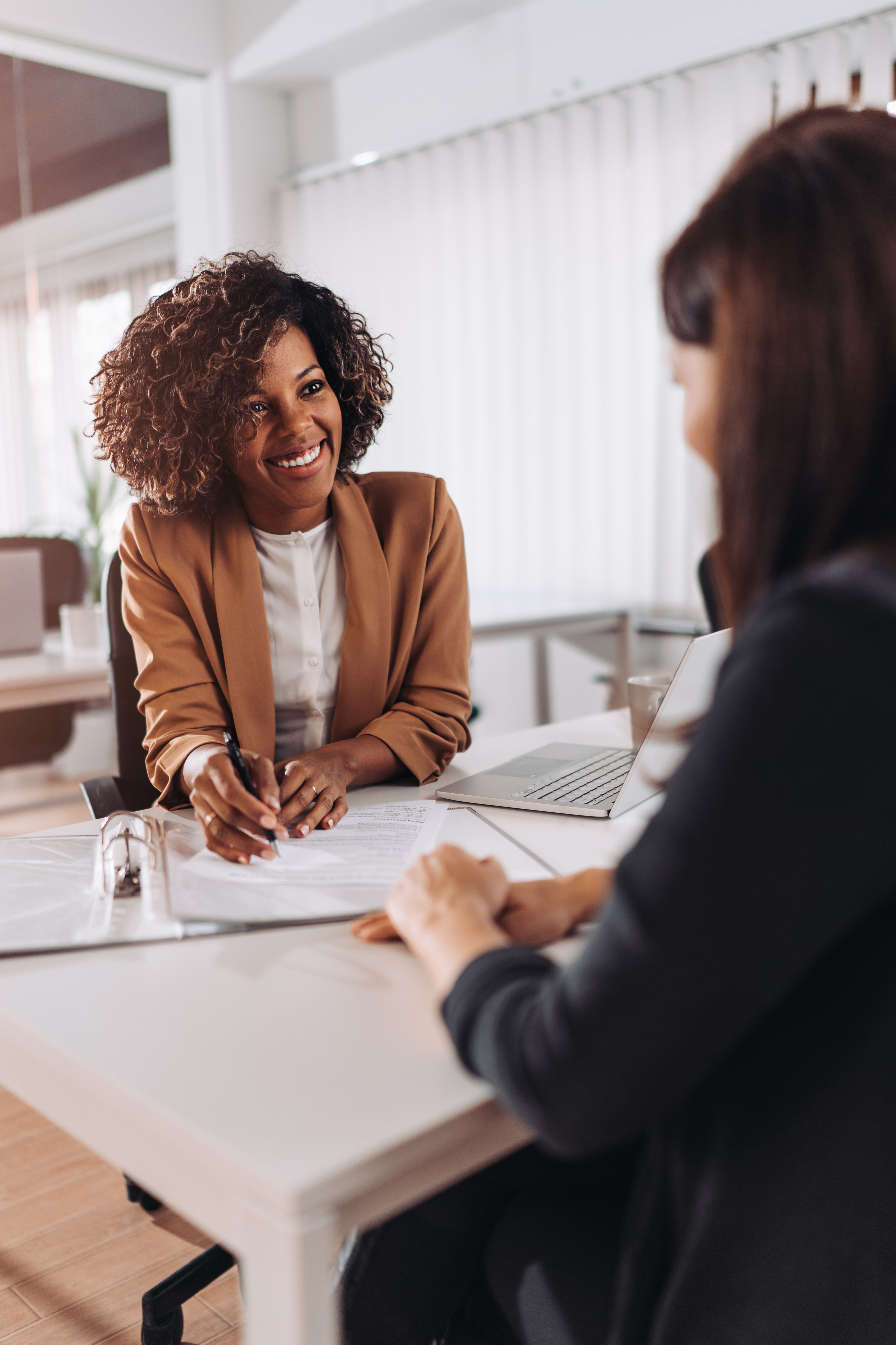 Smiling woman in a tan blazer leading a coaching consultation across a desk