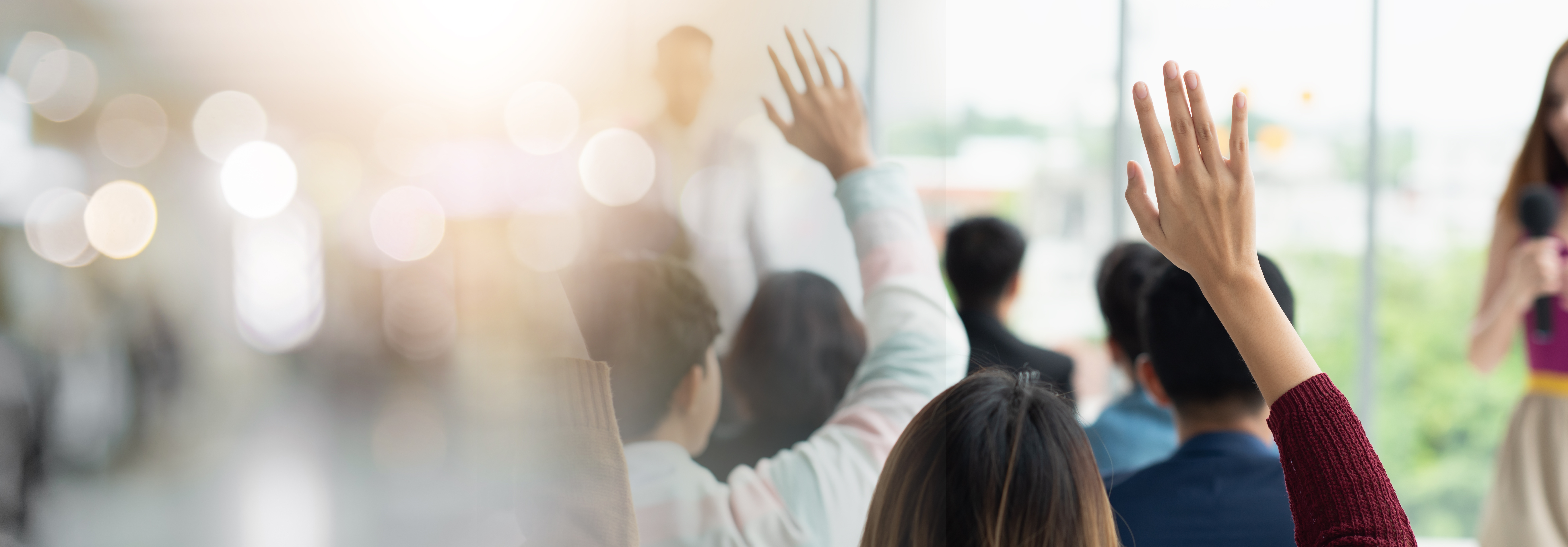 Audience members raising hands at a leadership workshop, photographed from behind