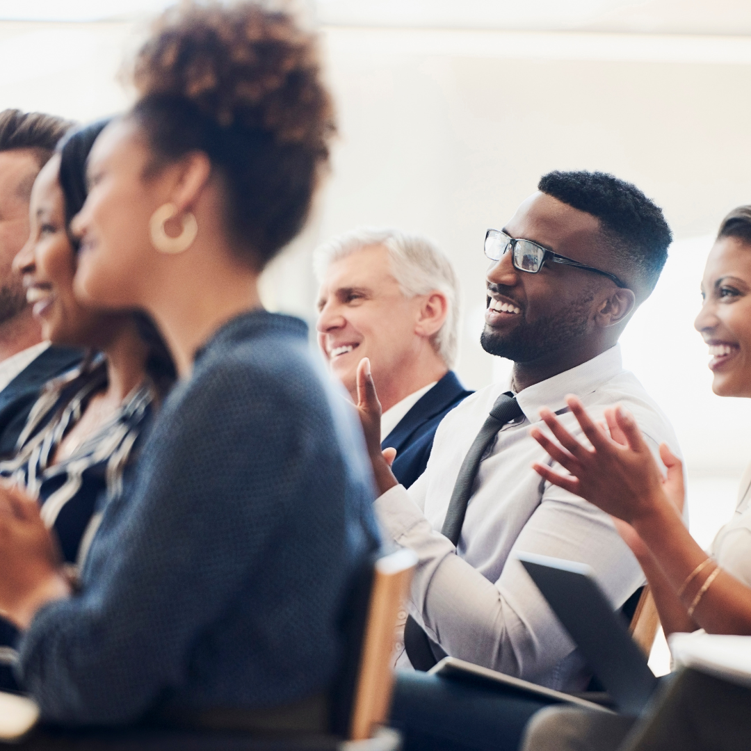 Diverse group of business professionals seated, applauding and laughing at a seminar